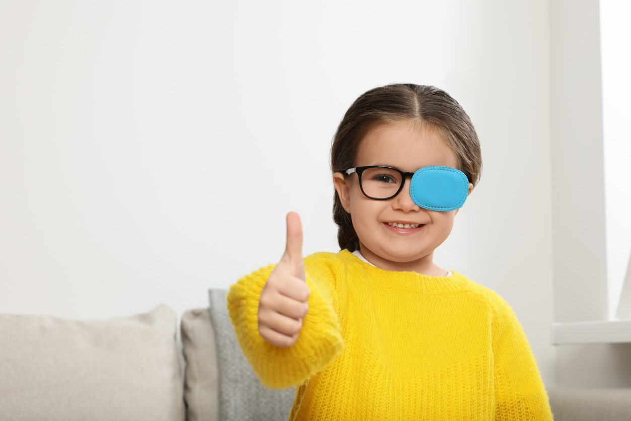 The image shows a young girl smiling and holding a thumbs up while wearing a patch over her glasses as she recovers from an orbital procedure. The image represents how long it takes to recover from orbital socket surgery.